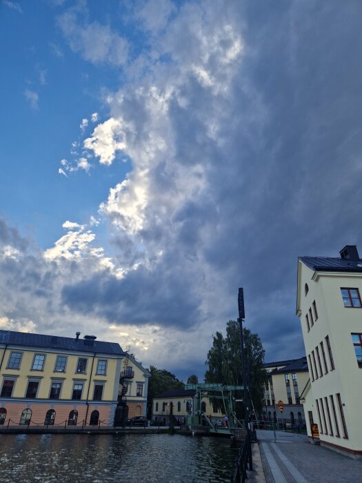 Gatulandskap vid kanal med historiska byggnader och dramatisk molnig himmel.