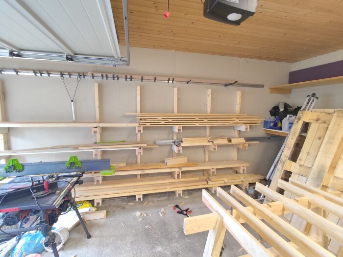 Hylla med träkonsoler och virkesförvaring i ett garage, verktyg och byggmaterial synliga i förgrunden.