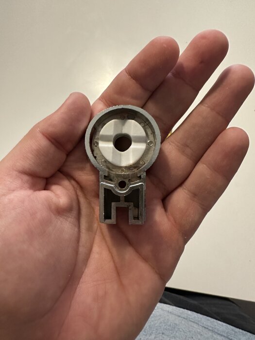 En hand håller en silverfärgad duschdörrsdel från märket Elsa, som används i duschdörrmekanismer.