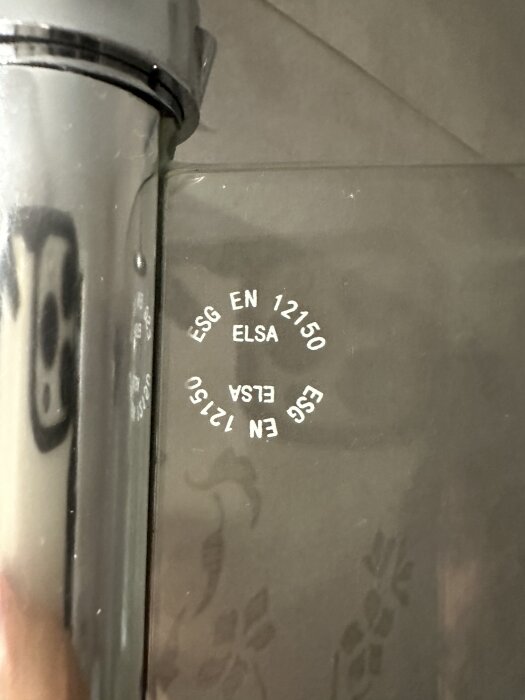 Duschdörr från märket Elsa med märkningen "ESG EN 12150" synlig på glaset bredvid ett metallhandtag.