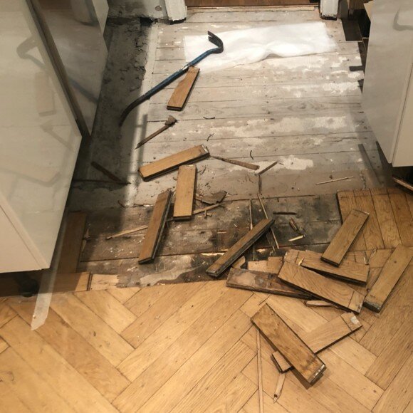 Borttagen parkett i kök, spridna plankbitar och en kofot på golvet.