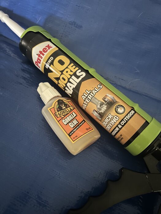 Två tuber lim, Pattex No More Nails och Gorilla Glue, ligger på en blå yta, använda för att försöka täta en presenning.