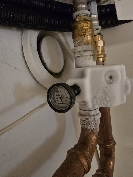 Frostat rör med termometer visar temperatur under 0 grader, del av frysprocess för 28mm rör. Vatten droppar fortfarande från röret.