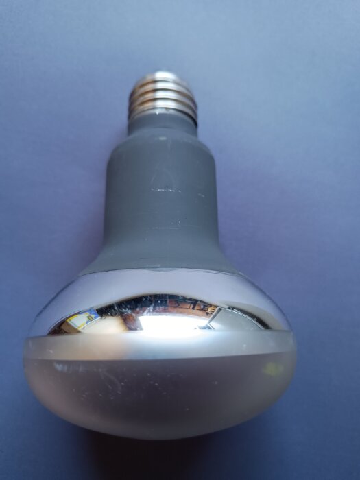 Lampa med spegelglasyta, konstruerad för kort livslängd men maximalt ljusutbyte, ligger på ett blått underlag.