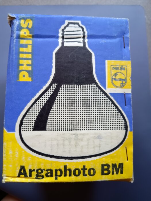 Förpackning med texten "Argaphoto BM" och en illustrerad bild av en glödlampa från Philips, designad för kort livslängd och maximalt ljusutbyte.