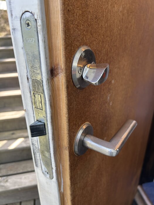 Närbild på en träytterdörr med ett metallhandtag och en Assa låskista.