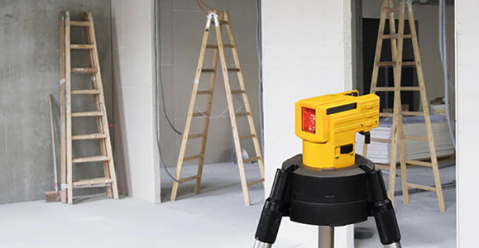 Självnivellerande krysslaser på stativ i ett rum med flera stegar i bakgrunden, används för bygg- och renoveringsprojekt.