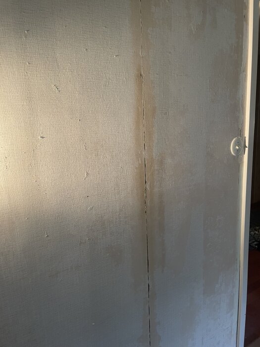 Vägg med avskalad tapet, synliga tapetskarvar och hål som ska spacklas.