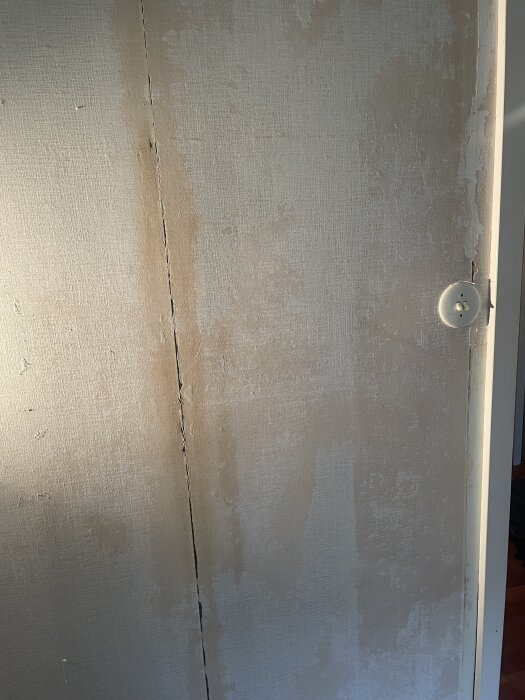 En gammal tapet med synliga tapetbårder och hål samt en bearbetad yta som är sandpapprad, med spacklingsarbetet ännu inte påbörjat.