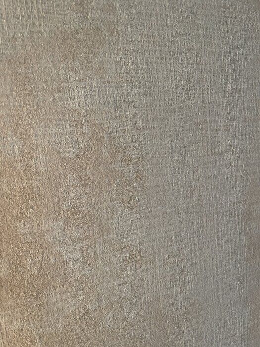 Yta av vägg med gammal tapet delvis borttagen, visar ojämn struktur innan spackling och slipning. Synliga spår av tidigare tapetbård.