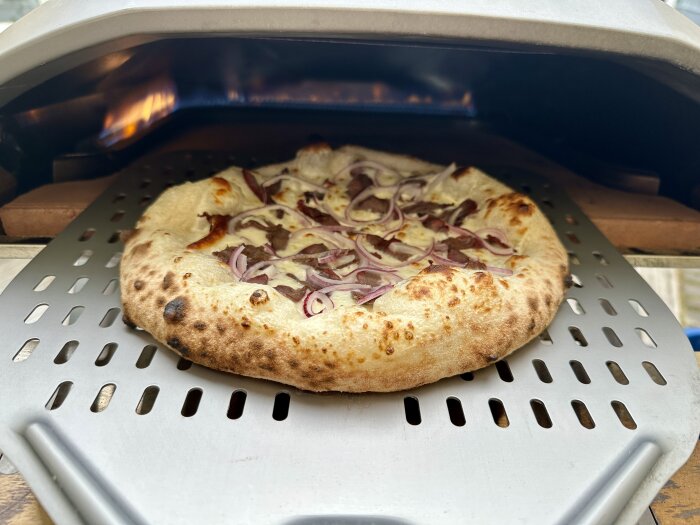 Pizza med rödlök gräddas i en vedeldad ugn.