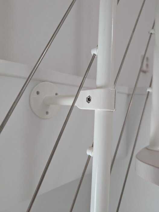 Vit trappa med tunn metallvajer och plastfäste monterad på väggen. Trappan tillhör en Fontanot Zen spartrappa till vinden.