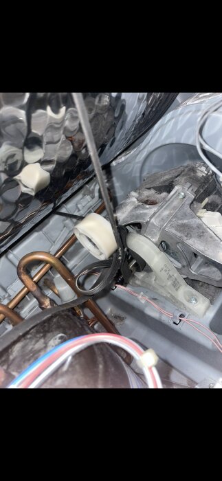 Nära bild av motorrem och remhjul med ett synligt löphjul och kopparrör i en maskin, möjligtvis en del av en apparat som har problem.