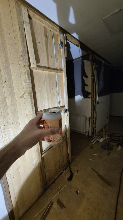 Renovering av hall, hand håller en ölburk och en vägg vid källartrappan inspekteras inför rivning.