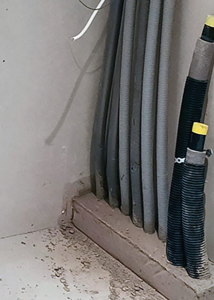 En vägg med flera kabelrör och kopplingar ovanpå en betongklack i ett hörn av ett rum.