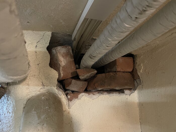 Hål i källarvägg med tegelfyllnad och synliga rör, från äldre hus. Fråga om röråtkomst och tätningslösningar diskuteras i forumtråd.