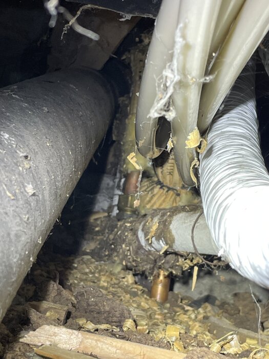 Rördragning med isolering och smutsigt område i källare, visar hål i väggen.