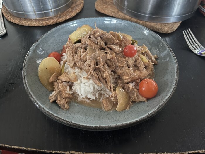 Tärnad skinkstek i gryta med ris och körsbärstomater serverad på en grå tallrik, stående på ett bord.