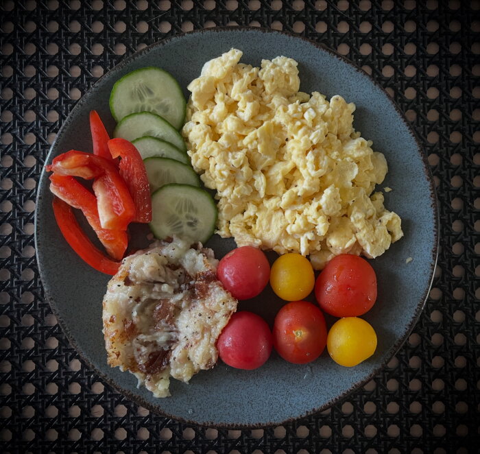 Scrambled eggs, cucumber slices, red pepper, cherry tomatoes, and leftover lapkojsbiff on a plate.