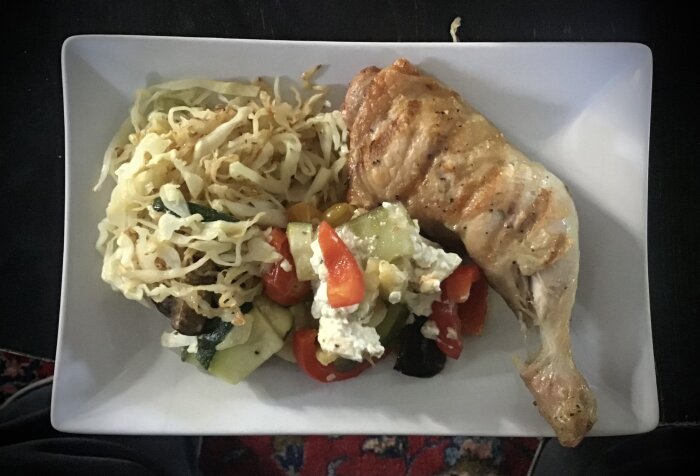 Grillad kyckling med ugnstekta grönsaker och fetaost samt stekt vitkål serverade på en vit tallrik.