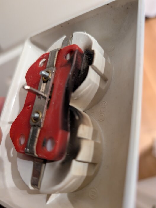 Närbild av ett eluttag med brända märken och svart beläggning runt kontakten som visar tecken på överhettning eller kortslutning.