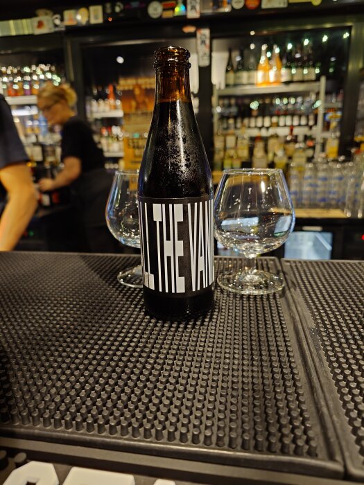 Flaska Omnipollo All the Vanilla med två glas på en bardisk, i en bar med flaskor i bakgrunden.