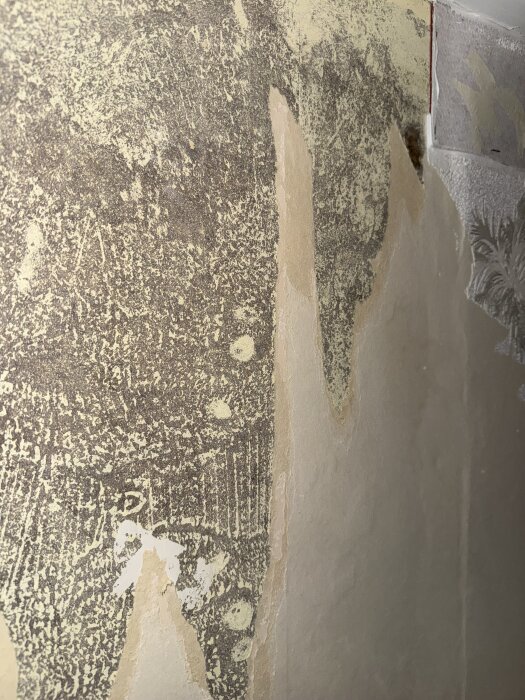 Närbild på gammal vägg med revor och olika lager av material exponerade, indikerar eventuellt asbestinnehåll.