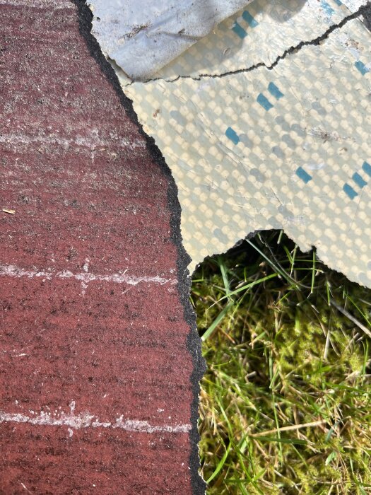 Rivet golv med röd och vit mönstrad yta, uppvisande sprickor och möjligt tecken på asbest, ovanpå gräsunderlag.