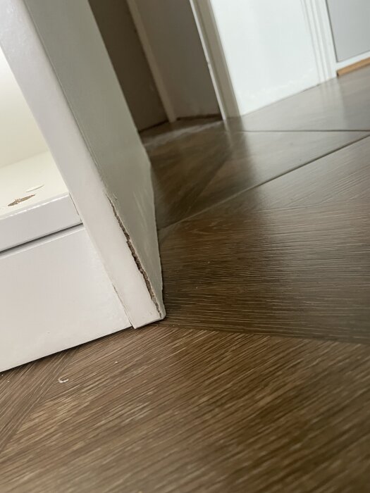 Kant på fuktskadad golvplatta och vägg i hall, visar vattenskador efter läckage.