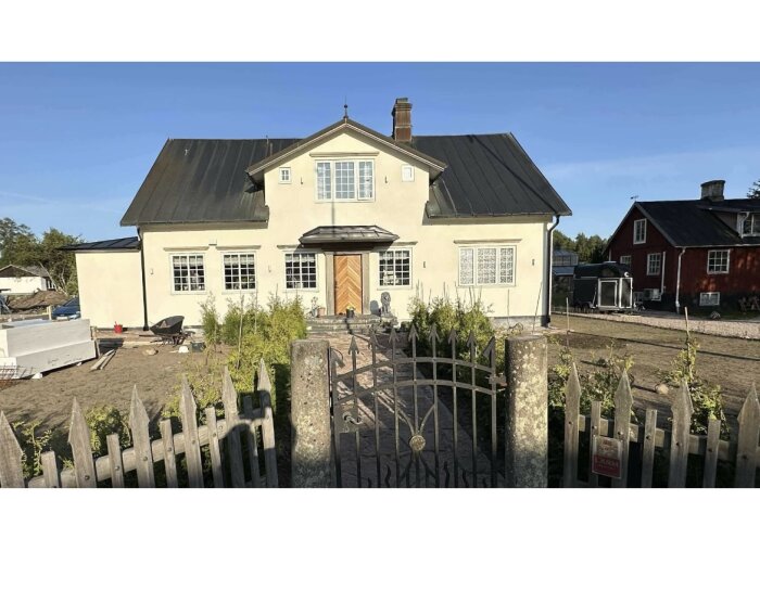 Renoverad 1800-talsvilla med ljus fasad, svart tak och en svängd trappa vid ingången. Framför huset syns en gård med en gammaldags grind.