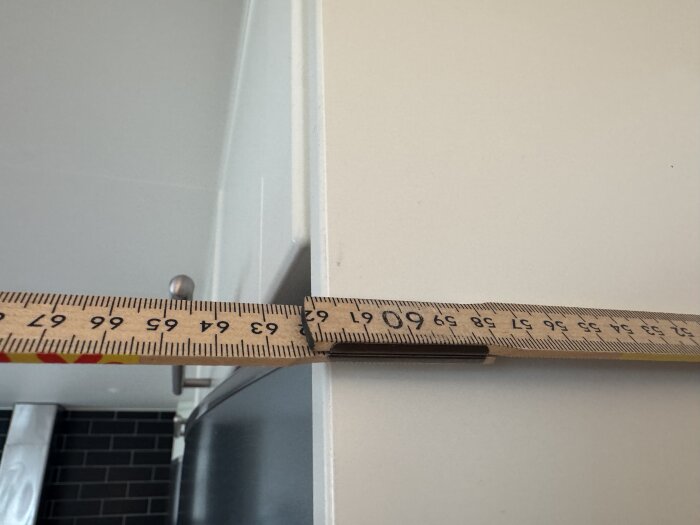 Måttstock som mäter djupet på en köksöverskåp som är 620 mm. Bakom syns del av en kökshandtag och ett skåp.