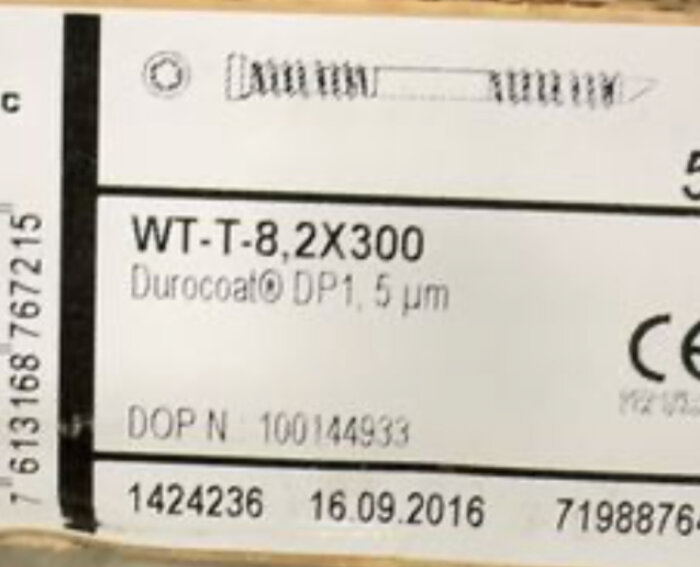 Etikett på en låda med skruvar, texten visar "WT-T-8,2X300" och "Durocoat DP1, 5 µm", tillsammans med streckkod och datummärkning.