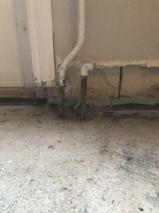 Vägg och golv visar exponerade rör bredvid en dörrkarm i ett rum under renovering efter vattenskada.