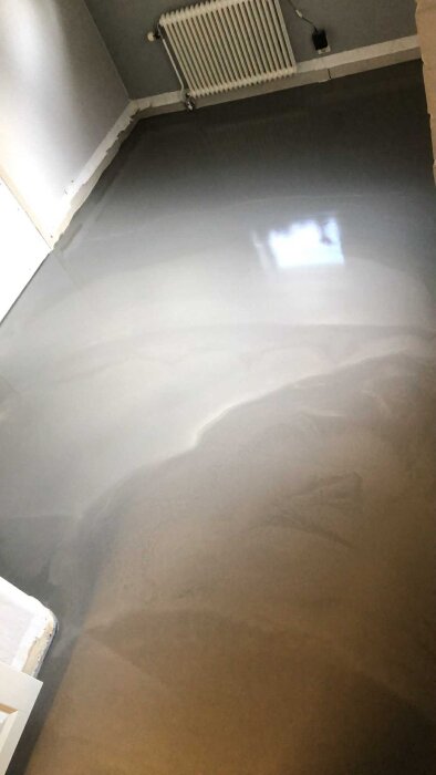 Nytt golv i rum med ljusgråa väggar, delvis borttagen golvsockel och vit radiator. Förberett för renovering efter elementläcka.