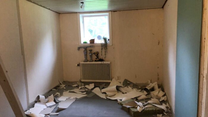 Rum med trasigt golv, utrivet väggmaterial och ett element under ett fönster. Verktyg och material på golvet.