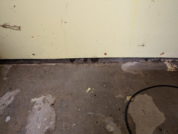 Fuktfläckar och vattenläckage vid nederkant av vägg och golv i gammalt garage, nära dörröppning, potentiell orsak till fuktskada.