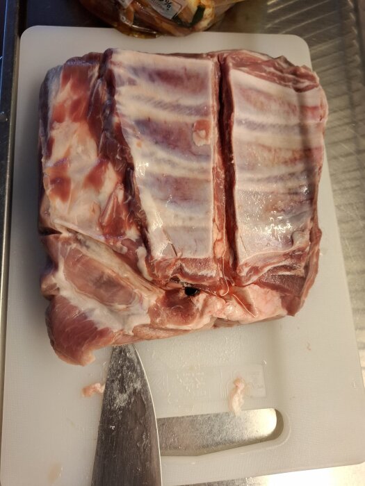 Ekologiska revbensspjäll på en skärbräda med en kniv, redo för marinering inför matlagning.