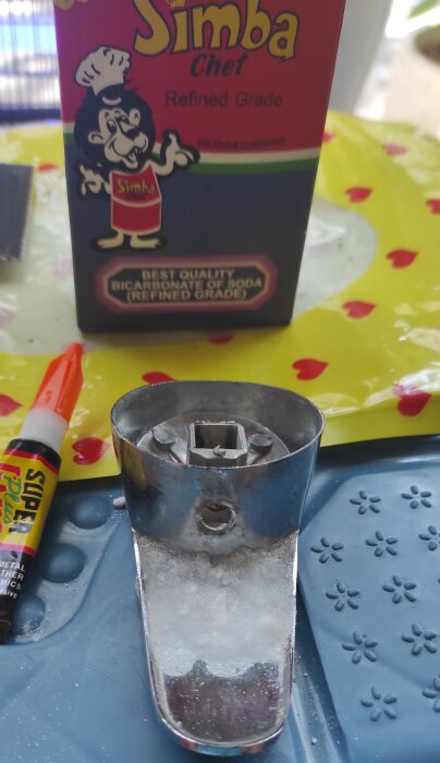 Avbrutet vred till tvättställsblandare med superlim och bikarbonat, bredvid en förpackning bikarbonat och limtub.