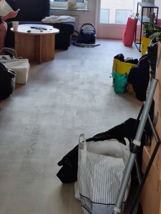 Ett vardagsrum med ekparkettgolv, sittgrupp, kaffebord och dammsugare. Golvet visar spridda fläckar och områden av ojämn slipning.