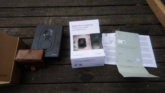 Förpackning och dokument för laddboxen "Zaptec Go 2" på ett träbord, inklusive en monteringsmall och bruksanvisning.