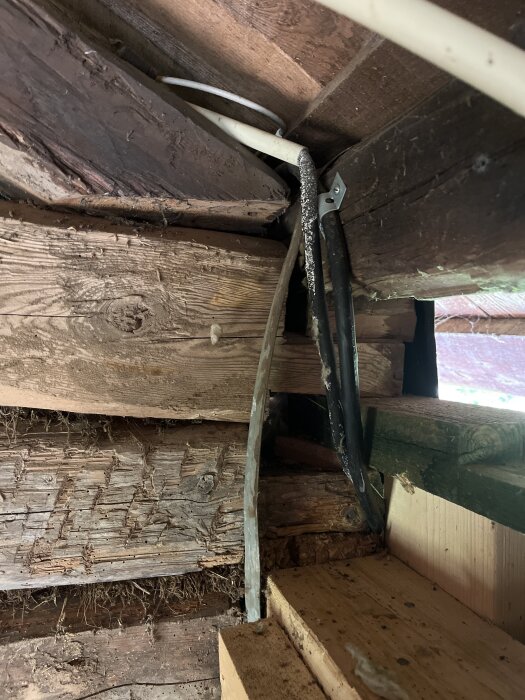 Gamla trästockar med synliga kablar och skarvar i en vägg hörn, del av en pågående renovering för att stabilisera gaveln.