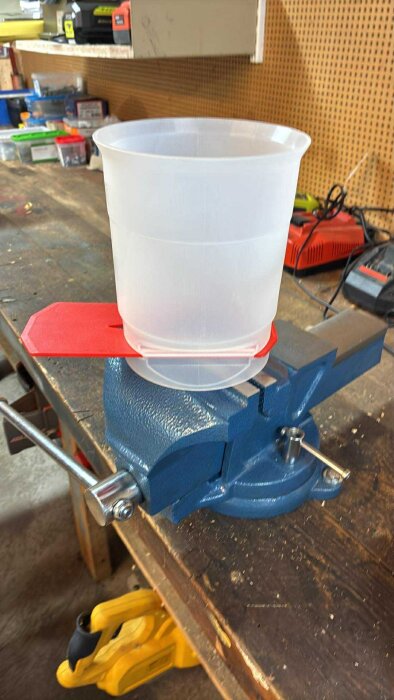 En genomskinlig plastbehållare på ett städs med ett rött lock, varvad i en verkstadsmiljö med verktyg i bakgrunden.