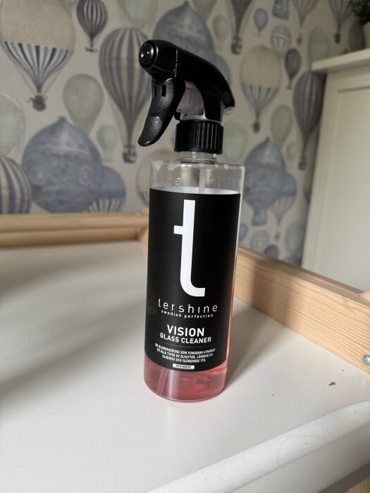 Flaska med Tershine Vision glass cleaner på en möbel framför tapet med luftballonger.