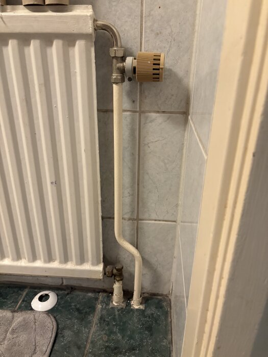 Ett element monterat på en vägg med röranslutningar synliga i ett badrum, inklusive en termostatventil och kakel på väggarna.