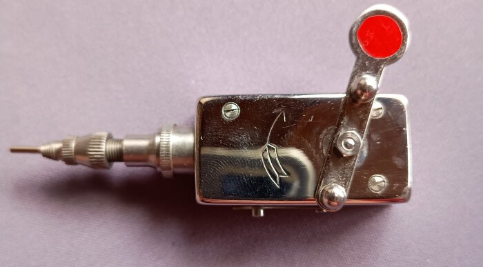 Mekanisk självutlösare av metall med en röd knapp, används för fotografering.
