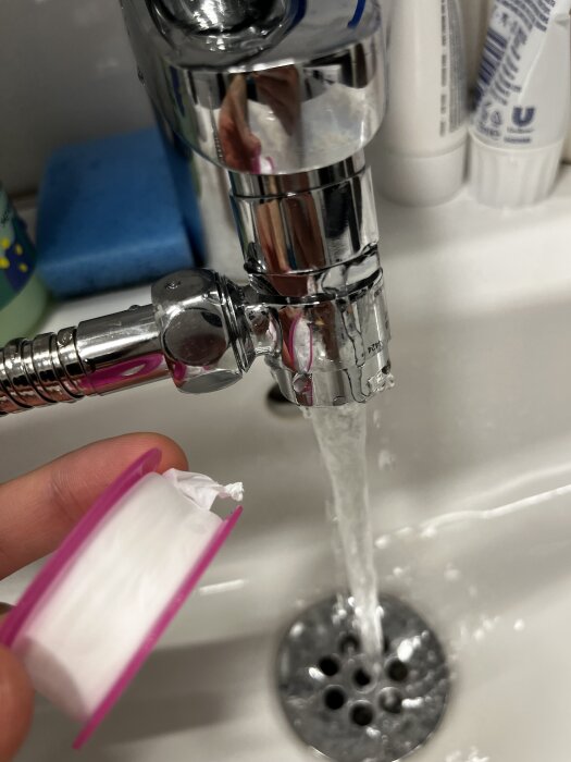 Kran med vatten som rinner och en hand som håller en rulle gängtejp ovanför ett handfat.