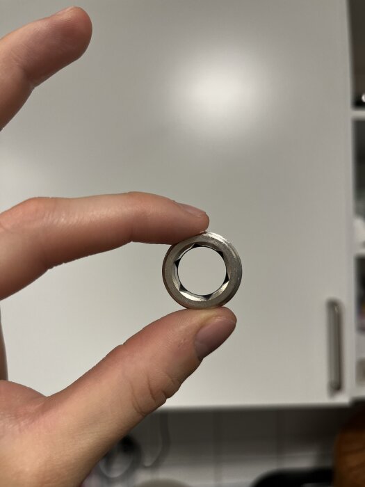 Sexsidig metallkoppling hålls mellan fingrarna, cirka 15 mm diameter, möjligen för insexnyckel, osäker på rätt verktyg.