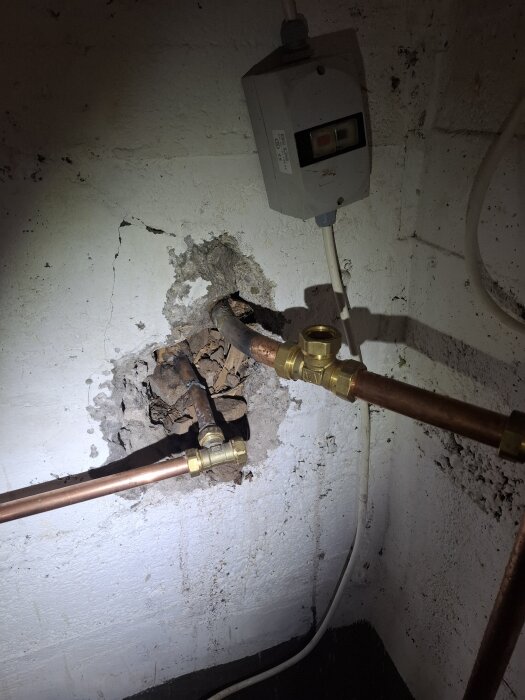 Vägg med kopparrör och en elbox, visar hur rören är kopplade genom en öppning i väggen.