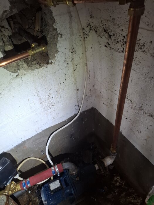 Vattenpump och kopparrör i en källare, med en väggöppning för rördragning.