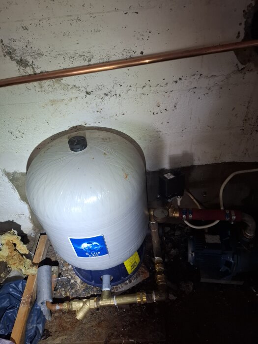 Vattenpump och trycktank i en källare med koppar- och rörledningar, del av en byggnadsinstallation.